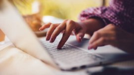 Close-up of female freelancer's hands typing on keyboard and working on laptop from home office